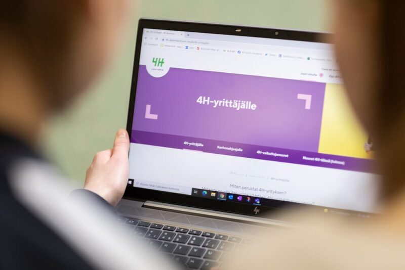 Lähikuvassa käsi pitelee kannettavaa tietokonetta, jonka ruudulla näkyy 4H-yhdistyksen kotisivu.